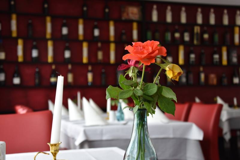Gedeckter Tisch mit Rose vor dem Weinregal